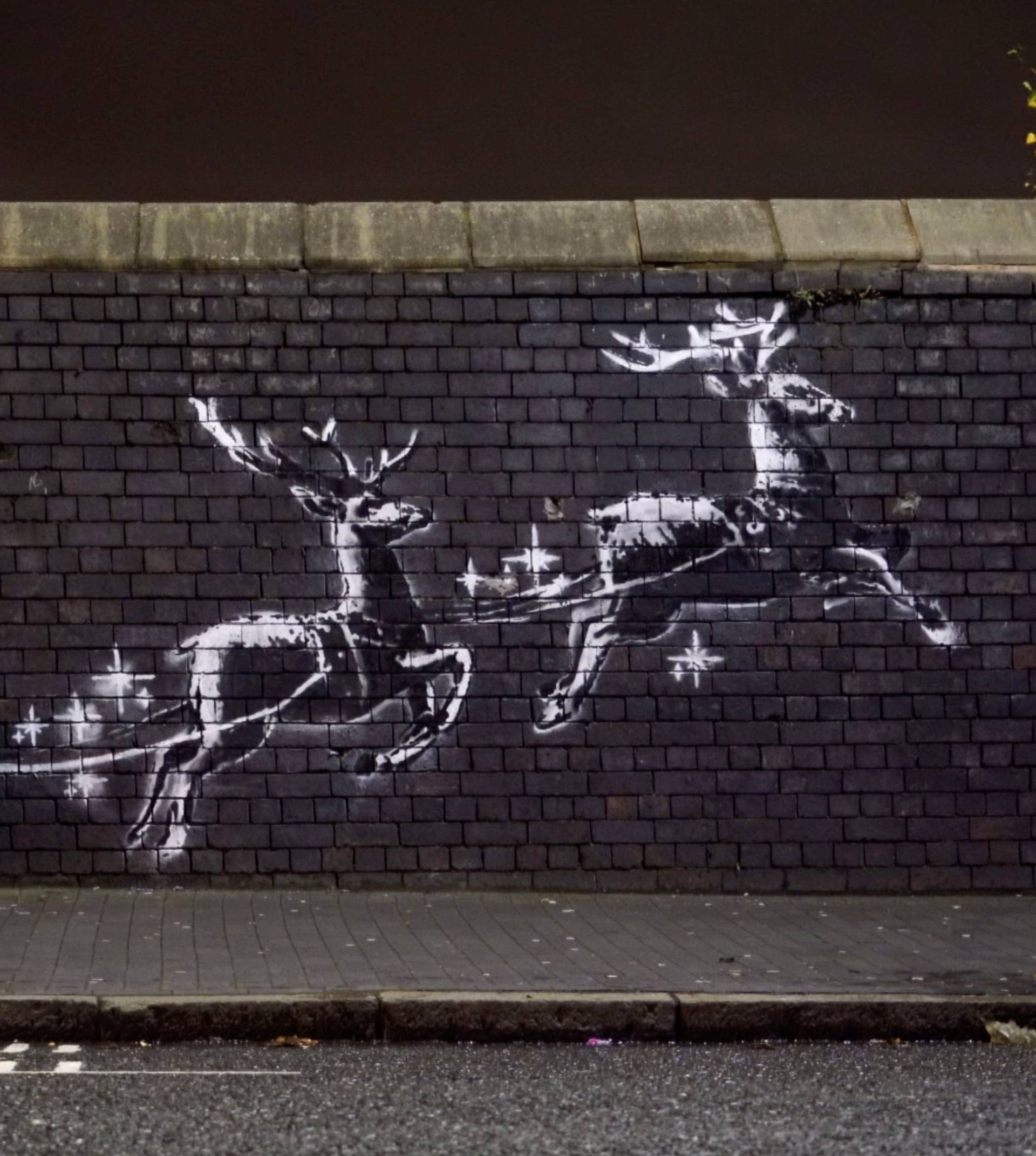 A man lays on a bench next to a new mural by Banksy in Birmingham