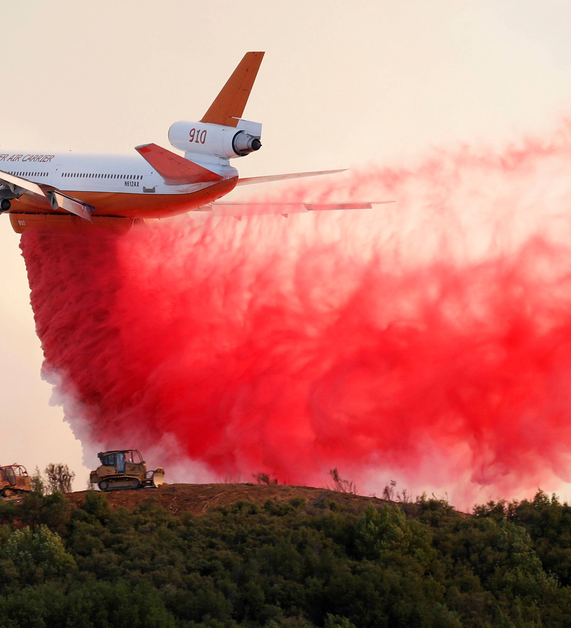 A DC-10 air tanker drops fire retardant along the crest of a hill to protect the two bulldozers below that were cutting fire lines at the River Fire in Lakeport, California