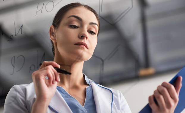 low angle view of scientist with felt pen near blurred formulas on glass board