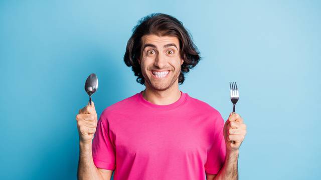 Portrait of nice funny cheerful guy holding in hands fork spoon preparing wait lunch isolated over bright blue color background