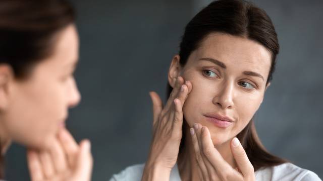 Close up unhappy woman looking at acne spots in mirror