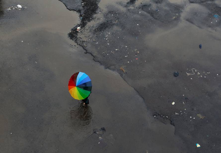 A woman carrying an umbrella crosses a flooded street as it rains in Mumbai