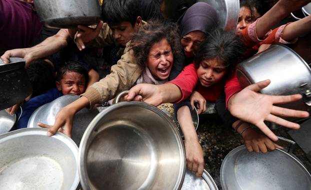 Palestinians wait to receive food cooked by a charity kitchen, in Jabalia