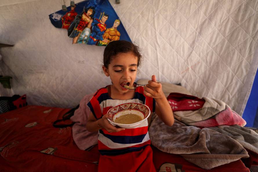 Eyala, the daughter of displaced Palestinian man Nizar Bakron, eats inside their tent, in Gaza City