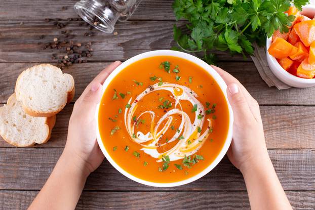 Kids hands holding a bowl with pumpkin soup on wooden background. Healthy eating concept. Top view.