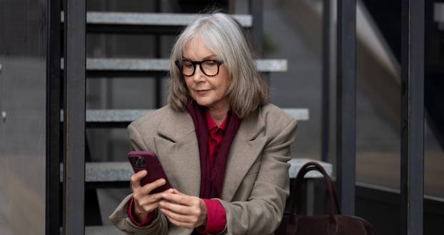 Middle-aged businesswoman in a trendy urban setting checking her smartphone while sitting on steps on a sunny day