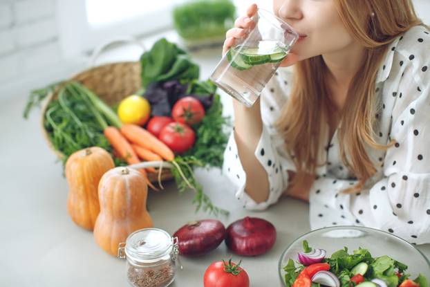 Woman on a diet. Young and happy woman eating healthy salad sitting on the table with green fresh ingredients indoors