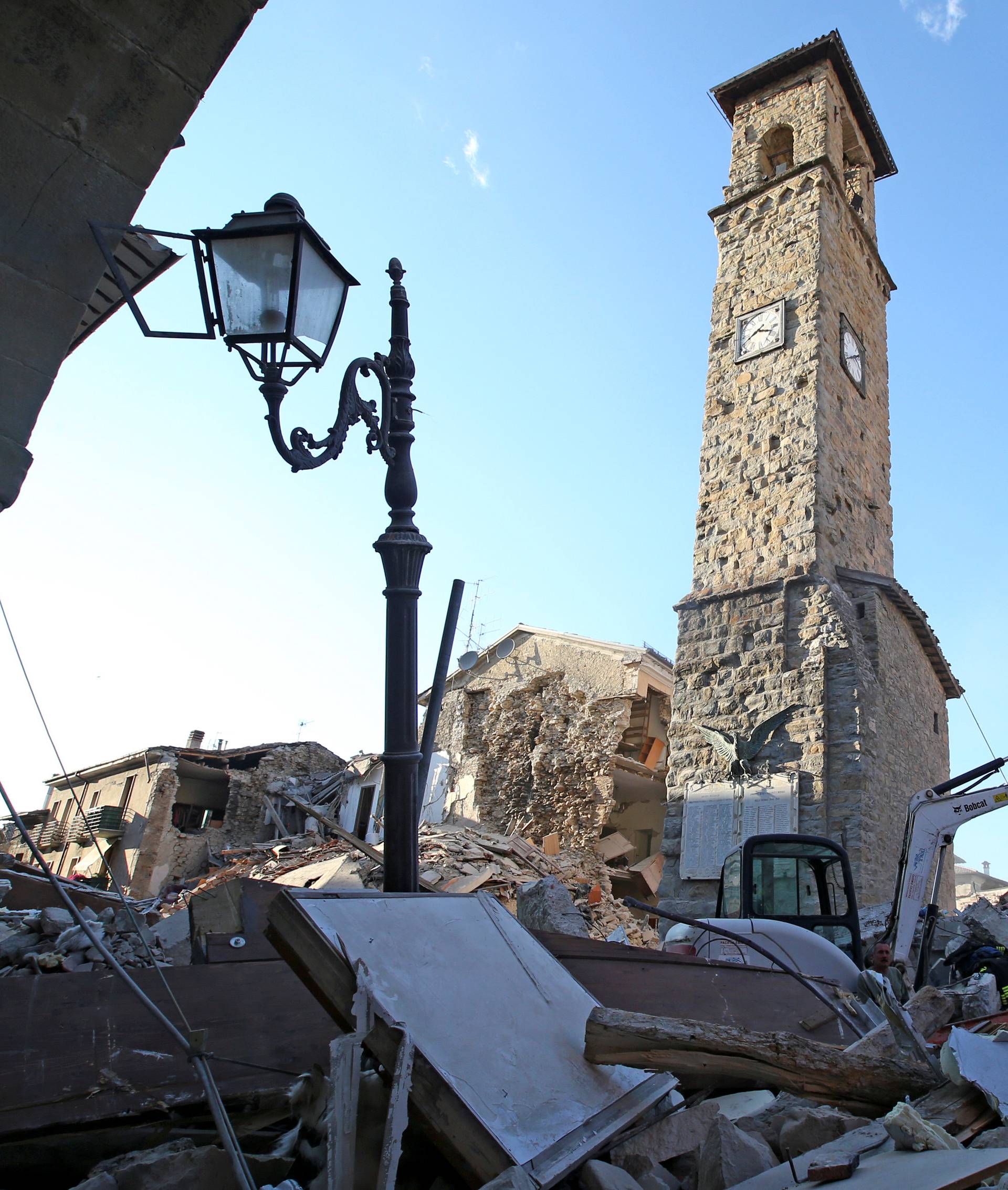 Rescuers walk past the bell tower with the clock showing the time of the earthquake in Amatrice