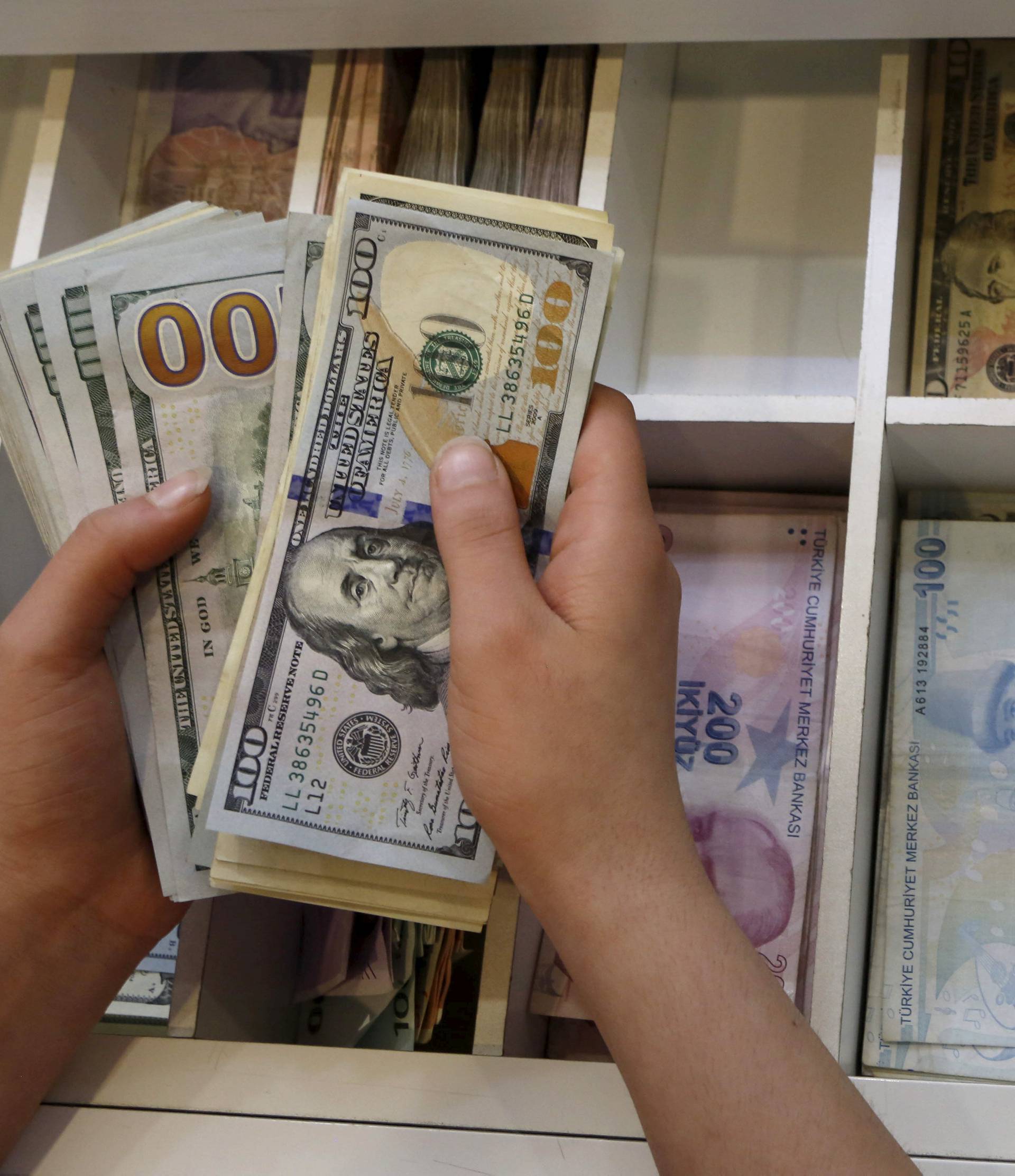 FILE PHOTO - A money changer counts U.S. dollar bills, with Turkish lira banknotes in the background, at an currency exchange office in central Istanbul