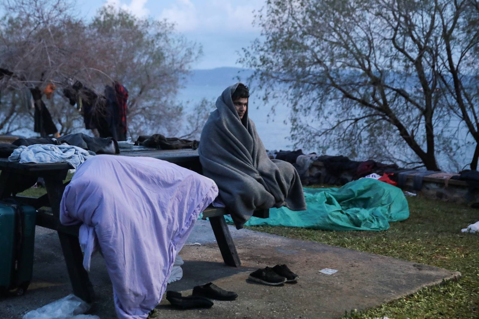 A migrant, who arrived the previous day on a dinghy after crossing part of the Aegean Sea from Turkey, sits covered with a blanket near the village of Skala Sikamias, on the island of Lesbos
