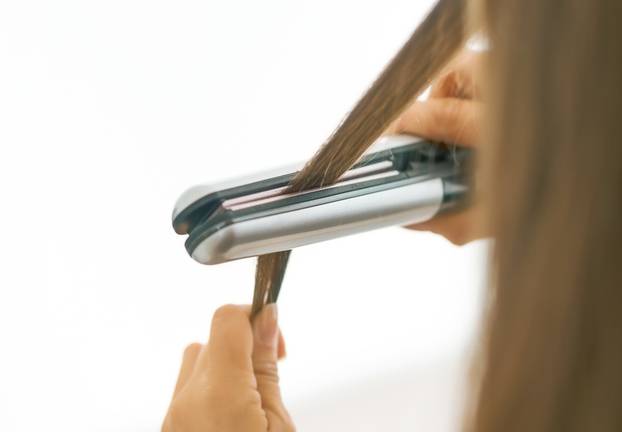 Closeup on woman straightening hair with straightener . rear view