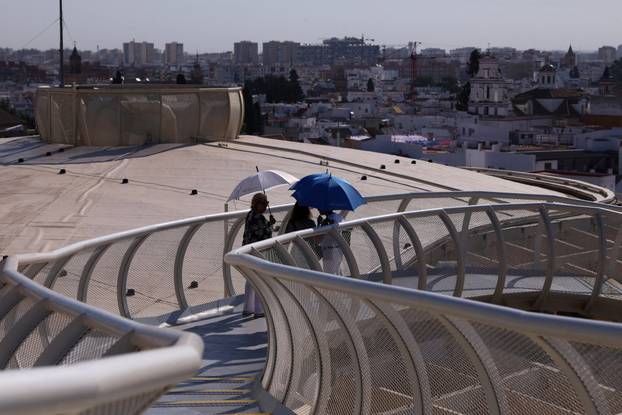 Tourists walk with umbrellas on Las Setas during a heatwave in Seville