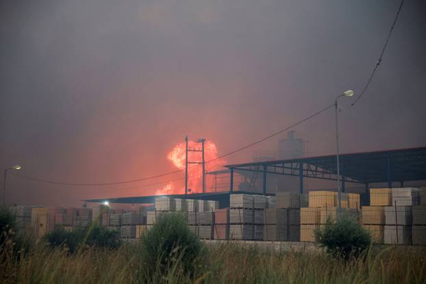 Flames rise from a cement factory sparked by a nearby wildfire, in Patras