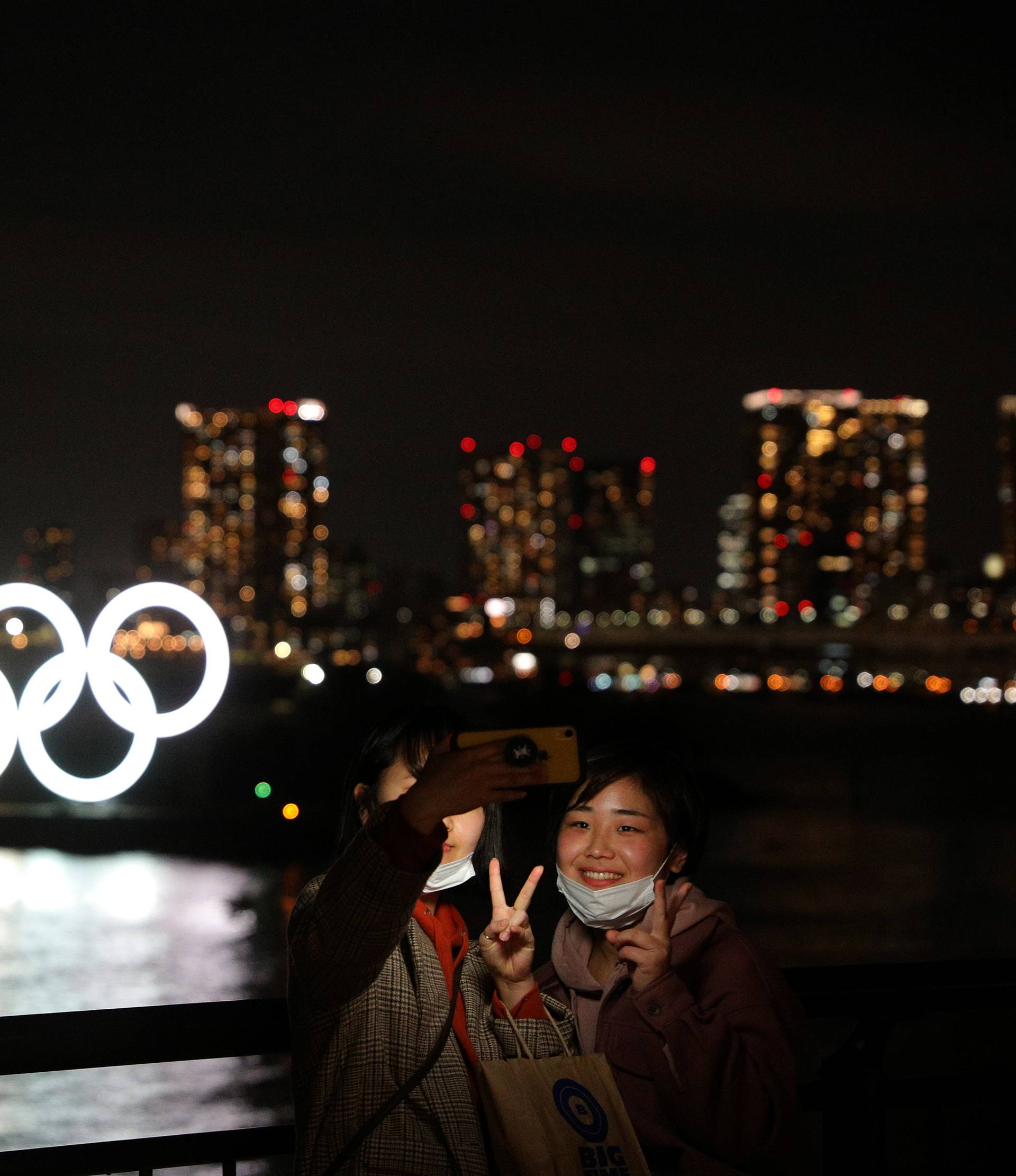 People take selfies in front of the giant Olympic rings at the waterfront area at Odaiba Marine Park in Tokyo