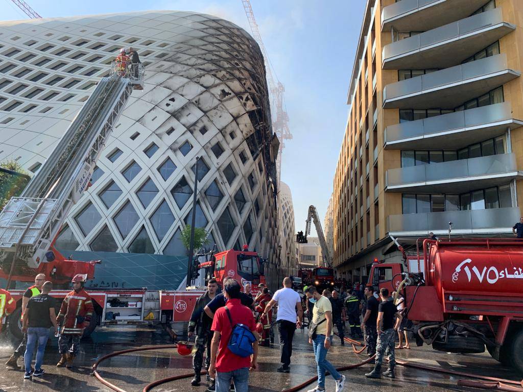 Firefighters and people gather near the site of a fire that broke out in a building in Central Beirut