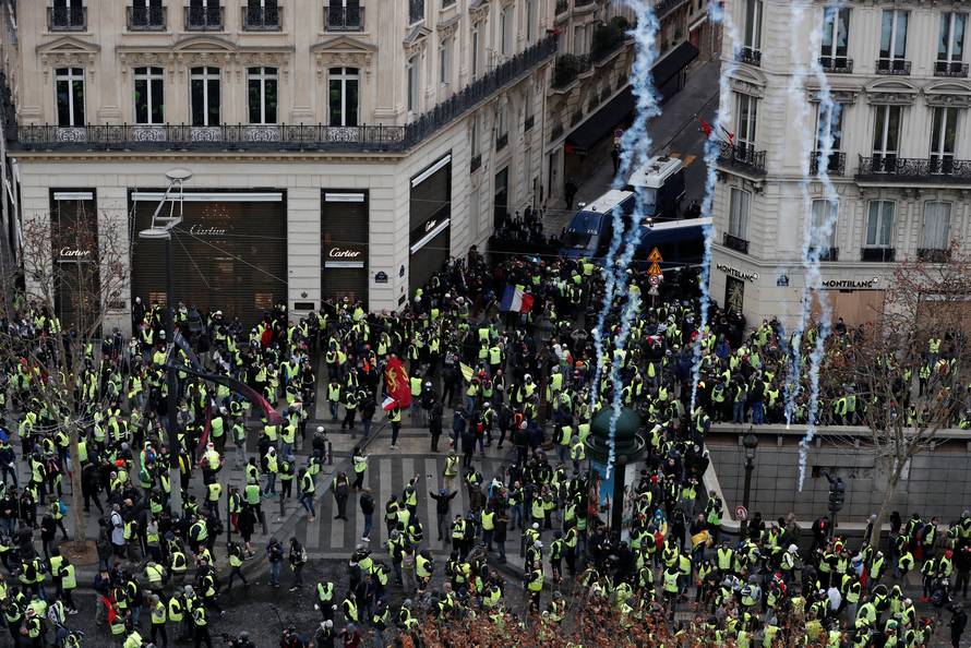 Tear gars floats in the air around protesters wearing yellow vests during clashes with French Gendarmes on the Champs-Elysees Avenue in Paris