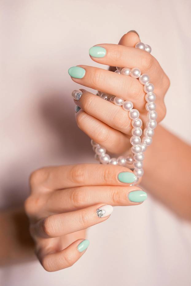 female fingernails with turquoise white french diamond manicure and pearl