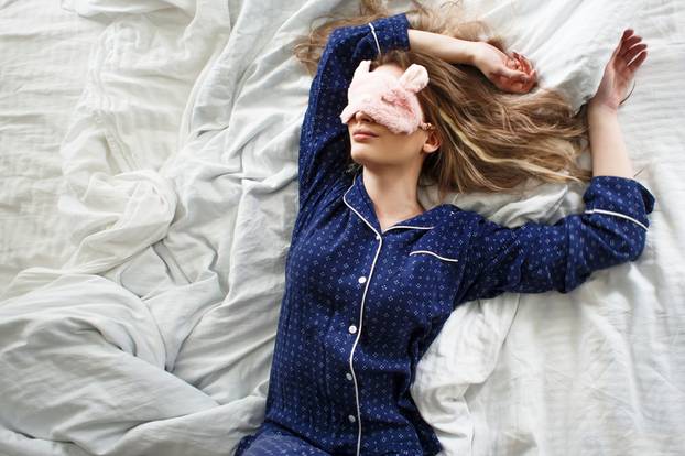 Cute blonde in her bed in blue pajamas and sleep mask, top view