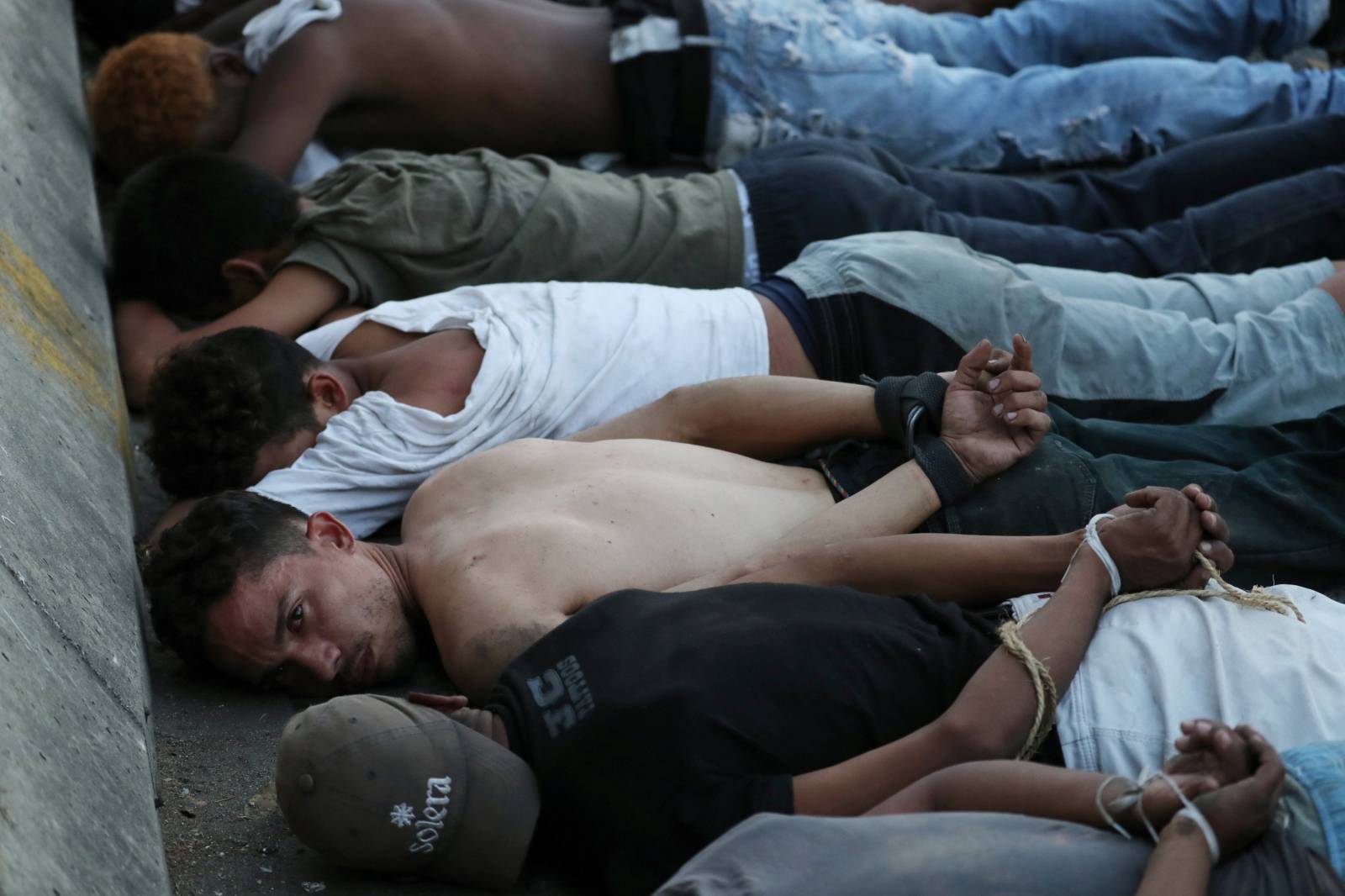 Men lie down on a street as they are detained by security forces after looting during an ongoing blackout in Caracas