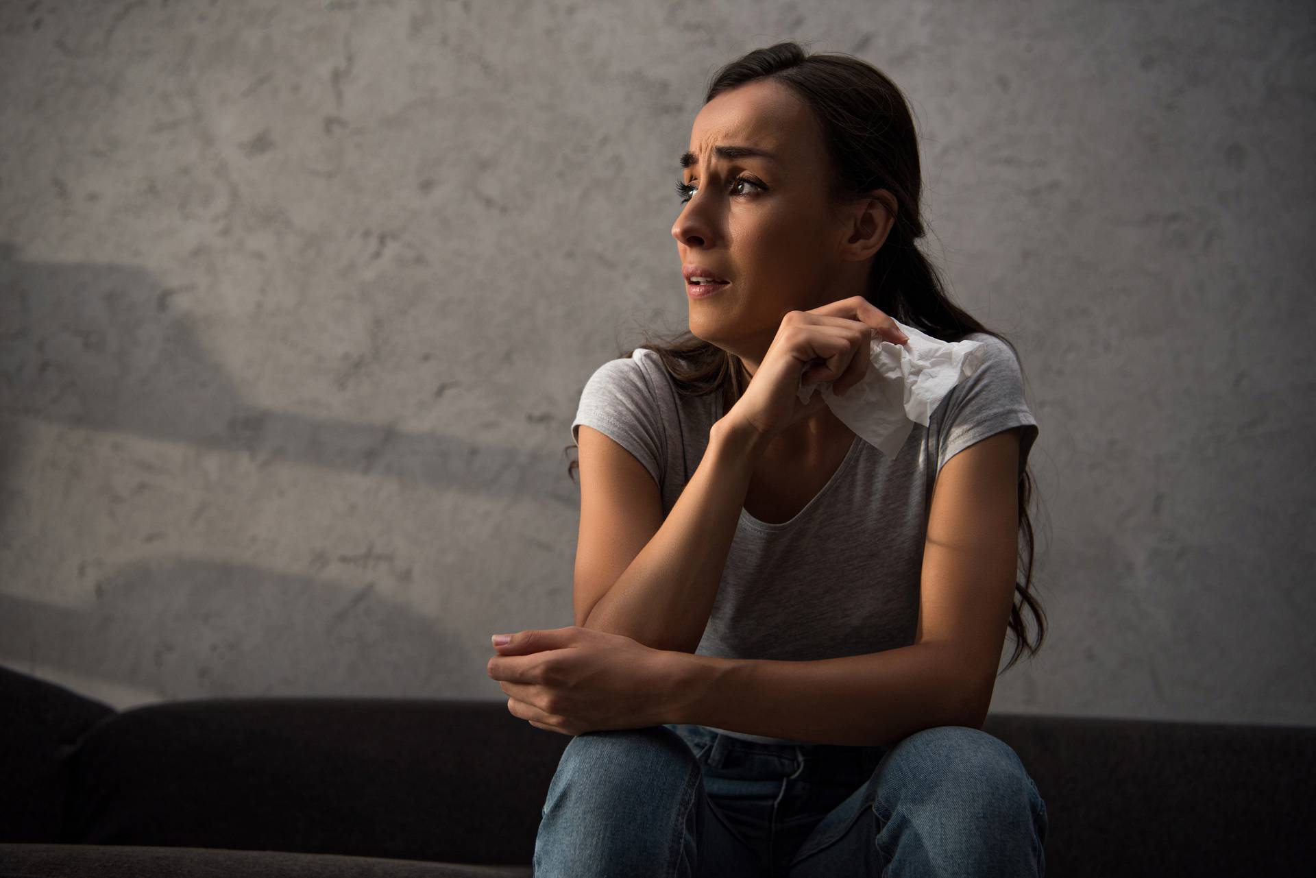 lonely crying girl holding napkin and sitting on sofa at home