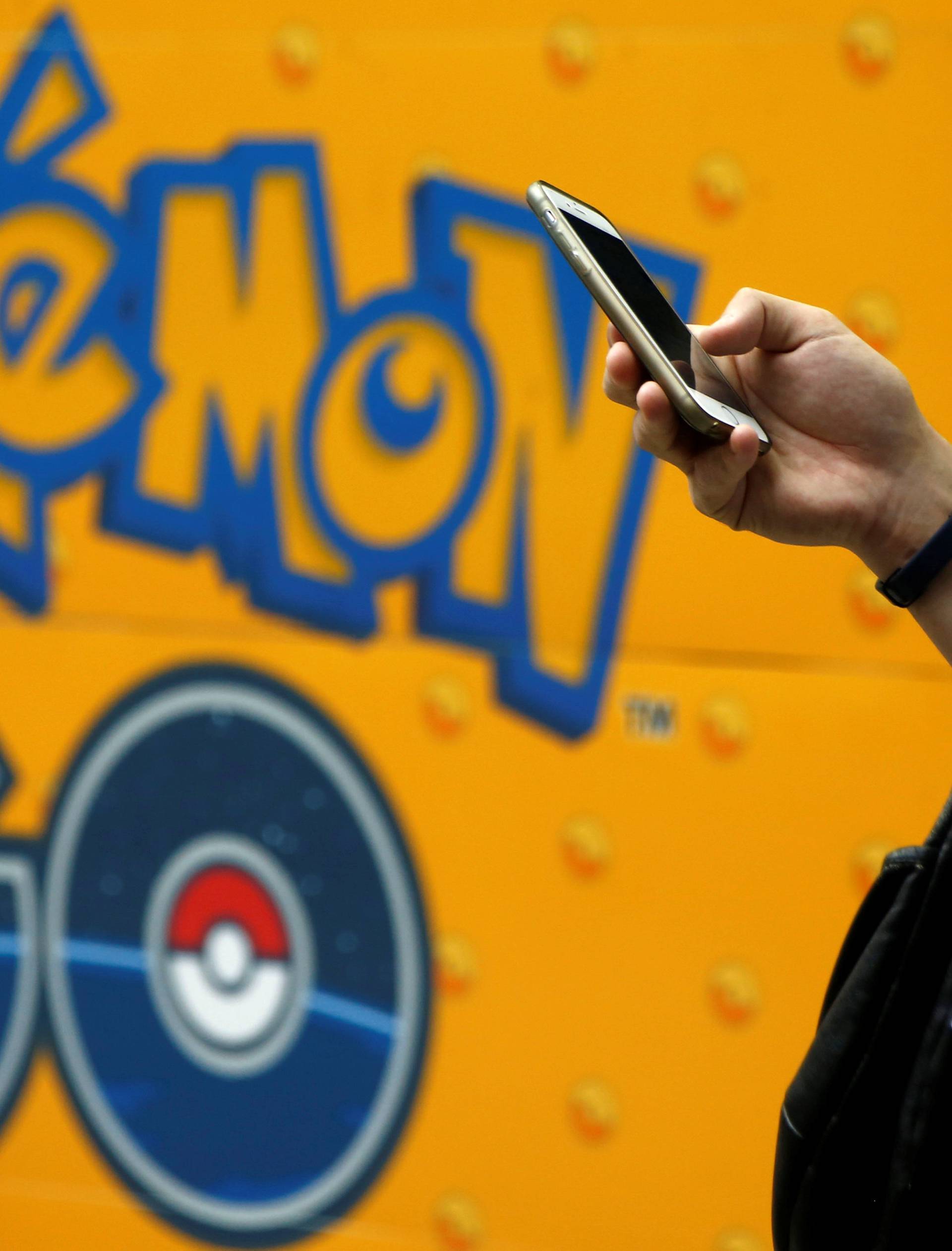 A man uses a mobile phone in front of an advertisement board bearing the image of Pokemon Go at an electronic shop in Tokyo
