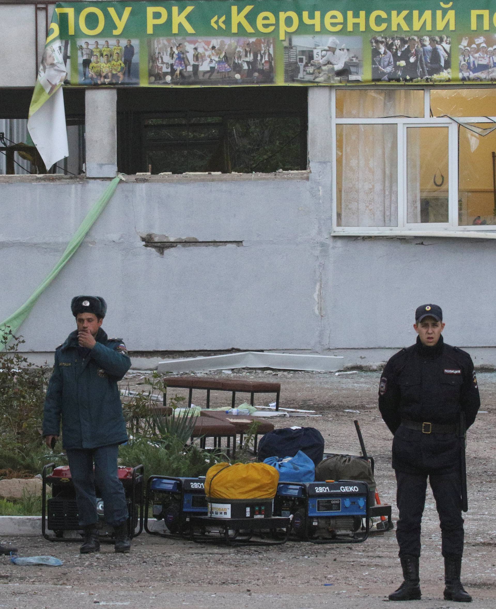 A Russian policeman and Emergencies Ministry members gather outside the damaged building of a college following a recent attack in Kerch