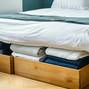 Under-the-bed storage drawers with neatly folded clothes, modern space-saving solution.