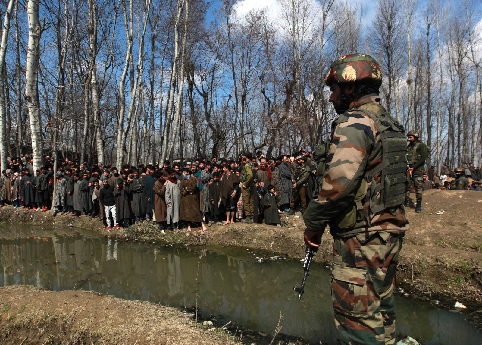 An Indian soldier stands guard as people look at the wreckage of Indian Air Force's helicopter after it crashed in Budgam