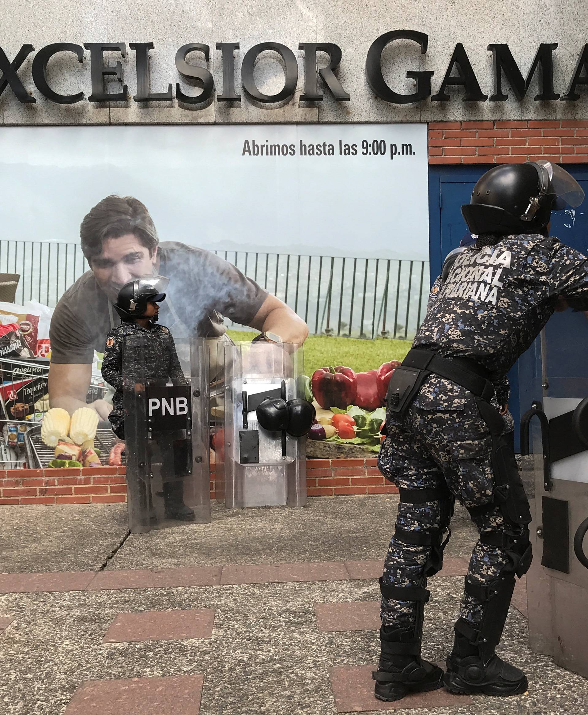 Police officers stand guard outside a supermarket in Caracas