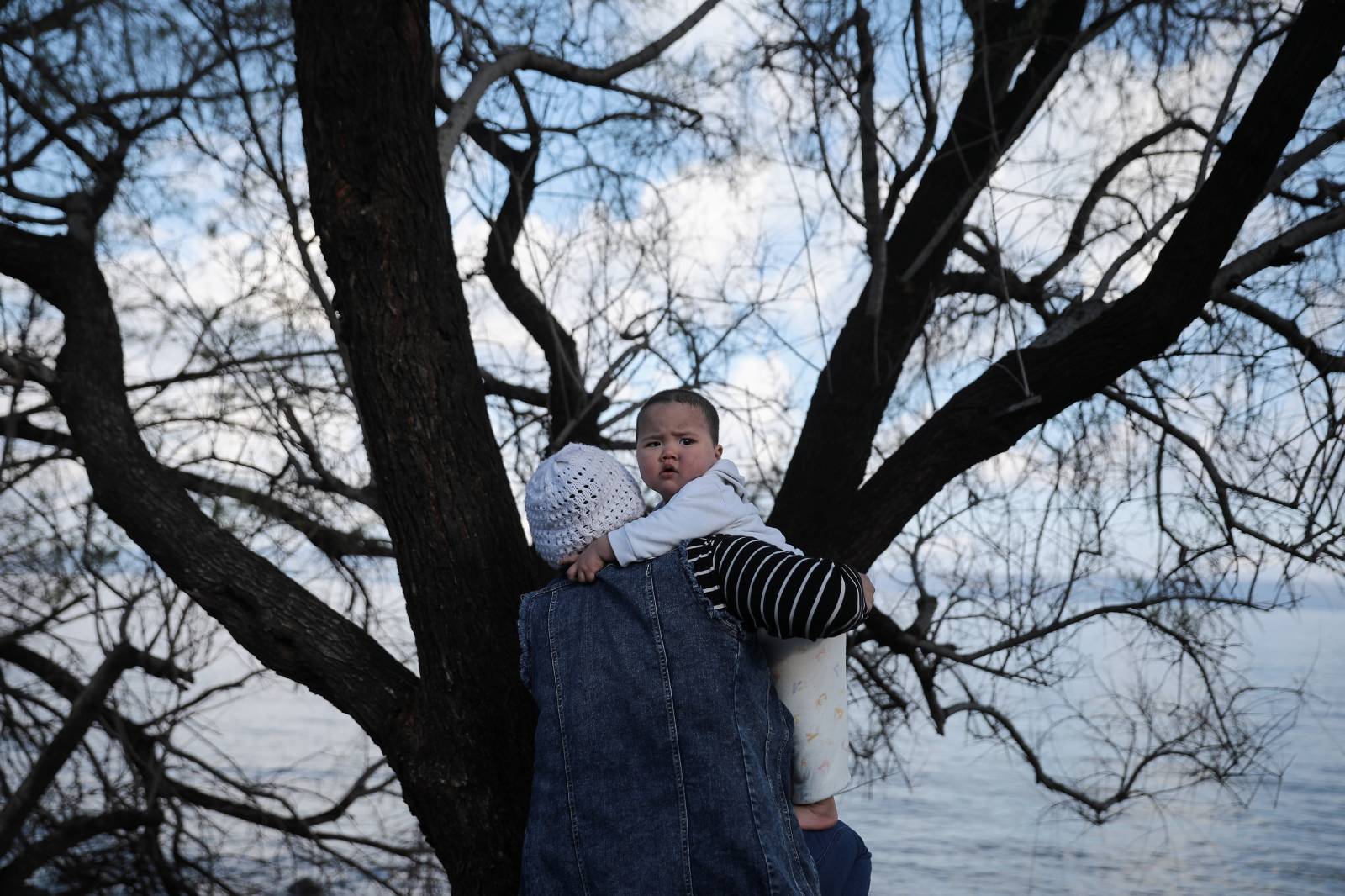 A woman holds a baby, as migrants who arrived the previous day on a dinghy after crossing part of the Aegean Sea from Turkey, are sheltered near the village of Skala Sikamias, on the island of Lesbos