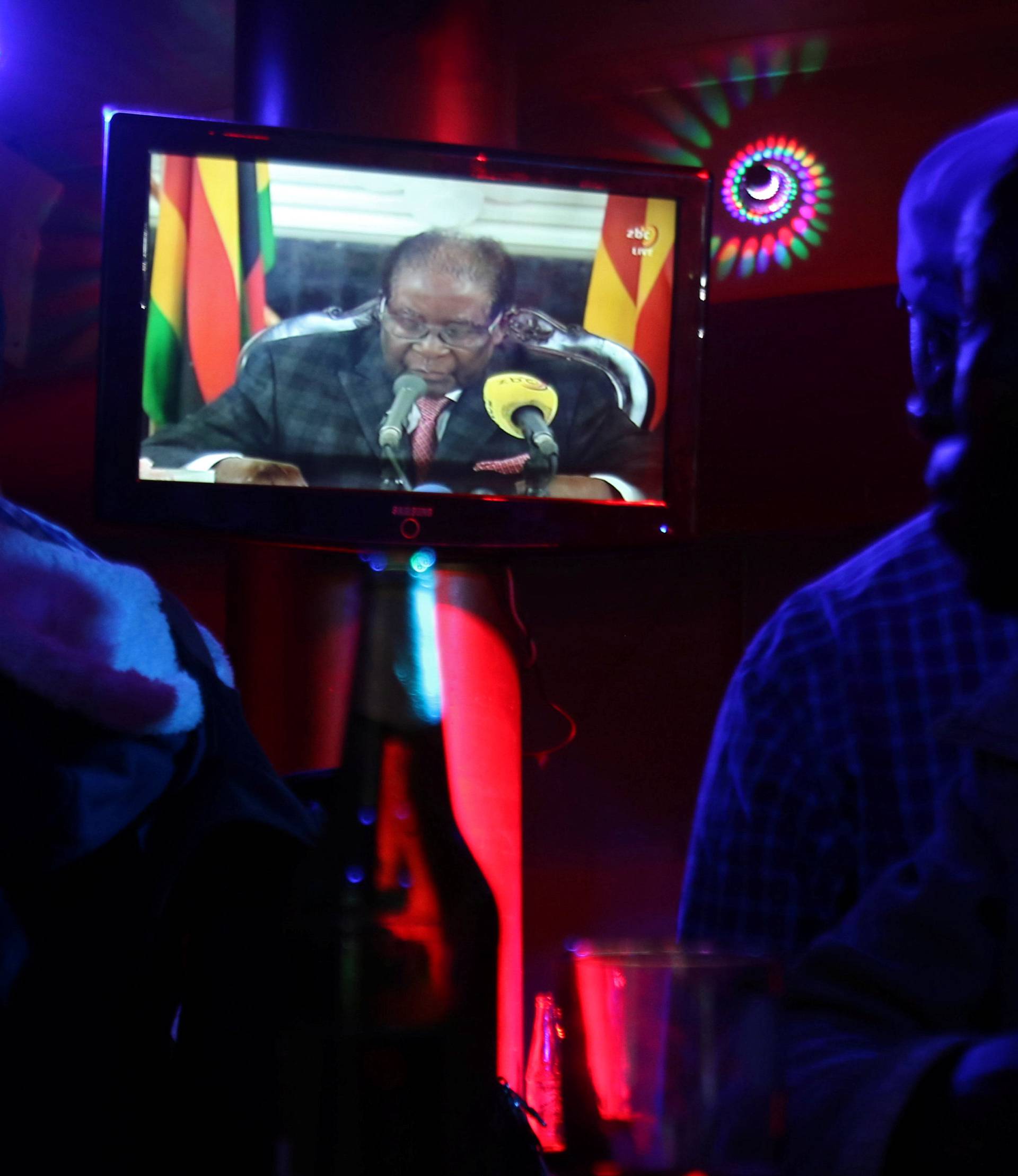 People watch as Zimbabwean President Robert Mugabe addresses the nation on television, at a bar in Harare