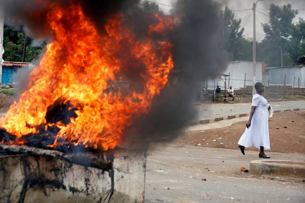 A woman walks past a burning barricades in Kisumu