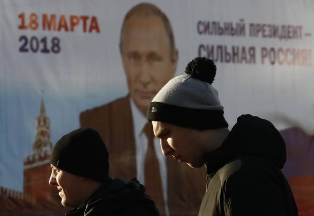 Men walk past a board, which advertises the campaign of Russian President Vladimir Putin ahead of the upcoming presidential election, in a street in Tula