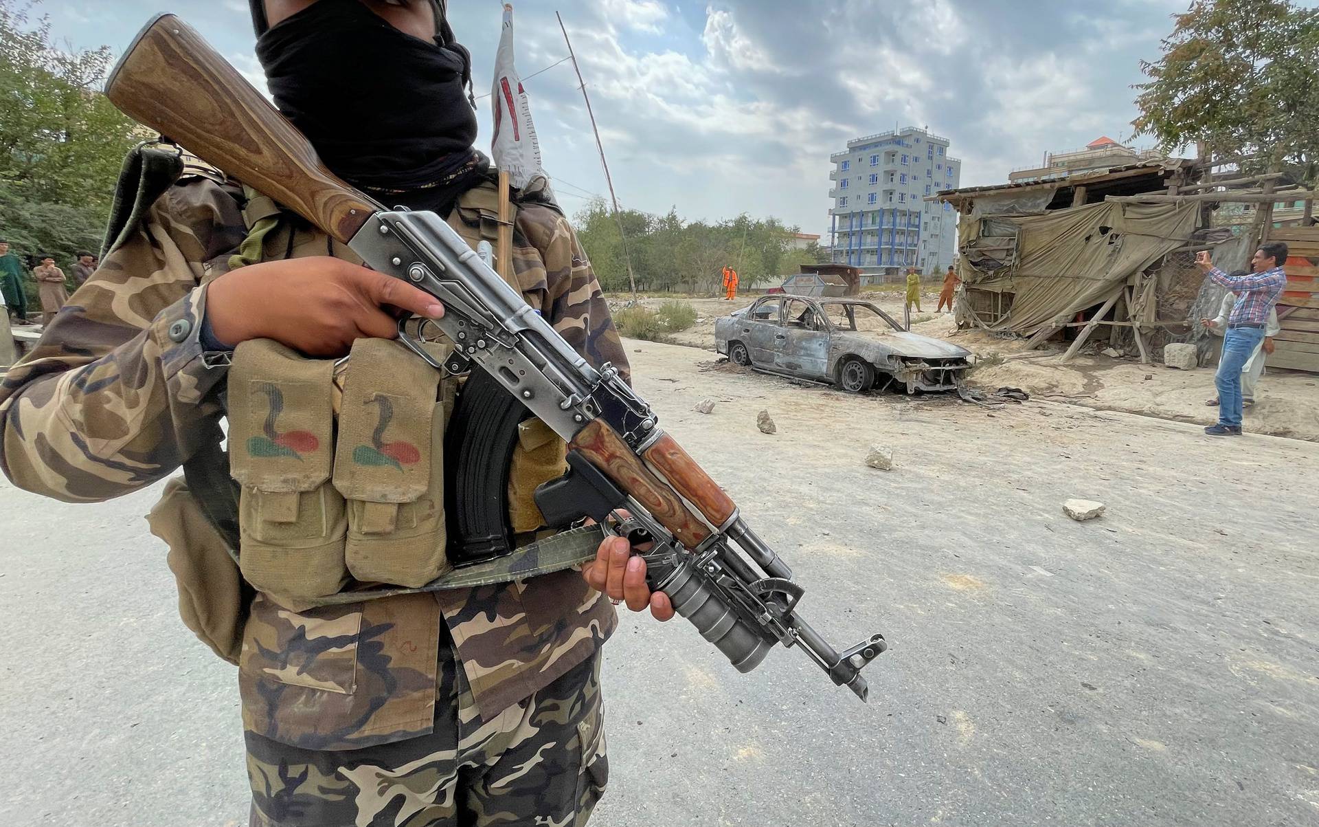 A member of Taliban forces stands guard as Afghan men take pictures of a vehicle from which rockets were fired, in Kabul