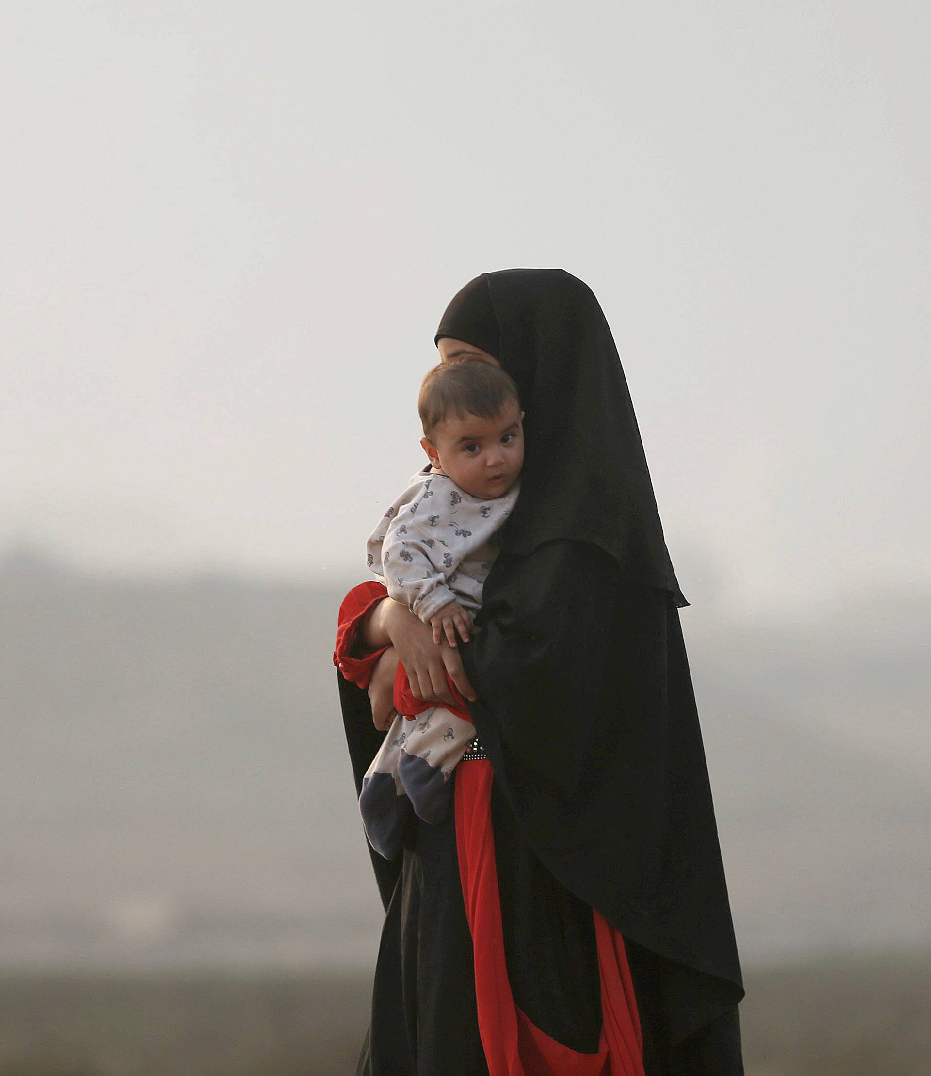 A newly displaced woman carries her child at a check point in Qayyara, east of Mosul