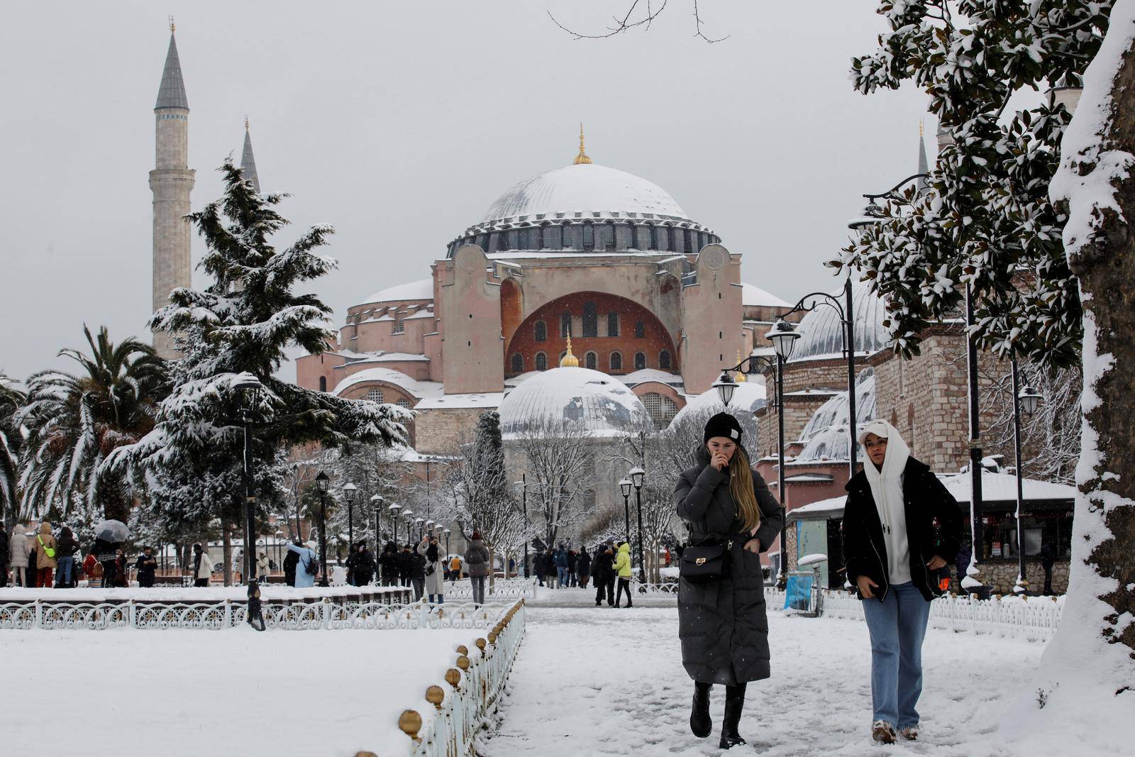 Tourists walk along Sultanahmet Square as Ayasofya-i Kebir Camii or Hagia Sophia Grand Mosque is seen in the background during a snowy day in Istanbul