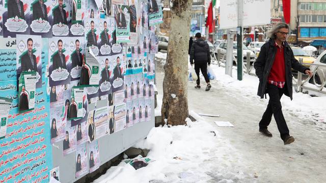 People walk past campaign posters for the parliamentary election during the last day of election campaigning in Tehran