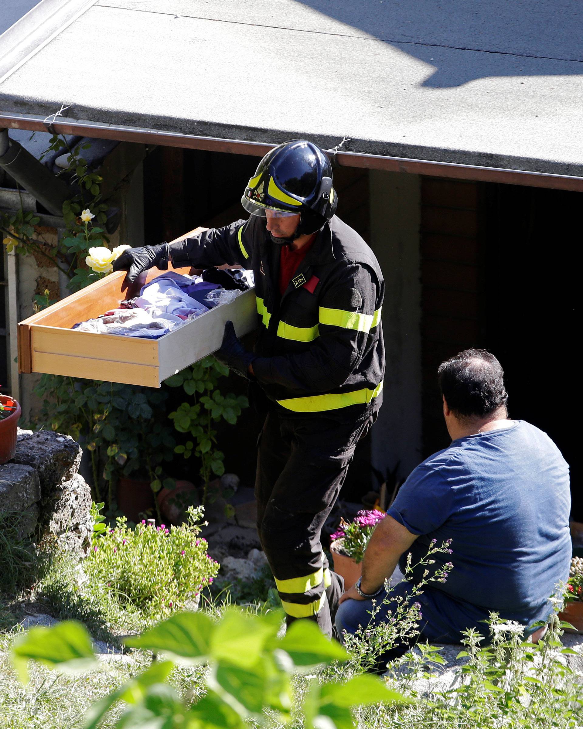 A firefighter takes out belongings from a man's house following an earthquake in Pescara del Tronto