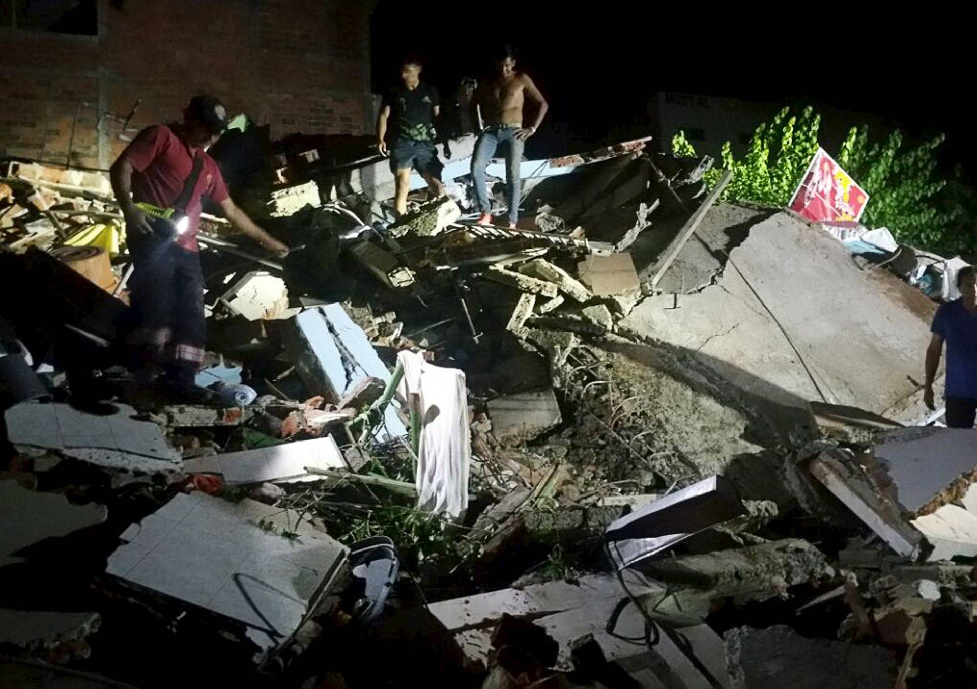 People stand next to the debris of a building after a 7.8 magnitude earthquake struck off the country's northwest Pacific coast causing "considerable damage", in Manta
