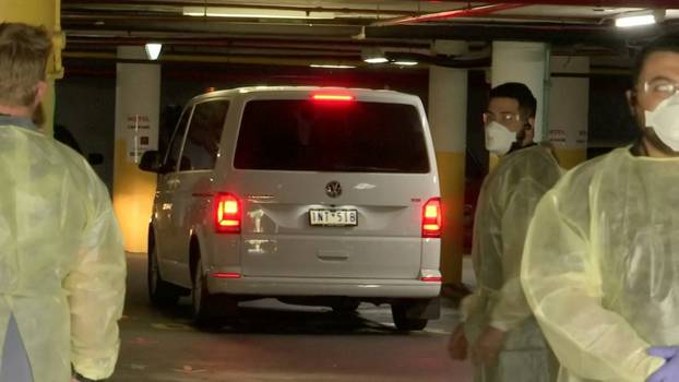 A van, presumedly holding tennis player Novak Djokovic, is surrounded by workers in personal protective equipment in a hotel carpark in Melbourne