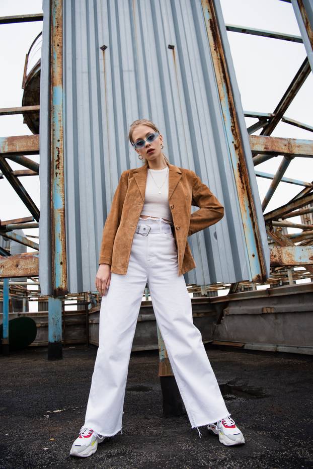 full length of pretty young model in blue sunglasses posing with hand on hip near rusty construction on rooftop
