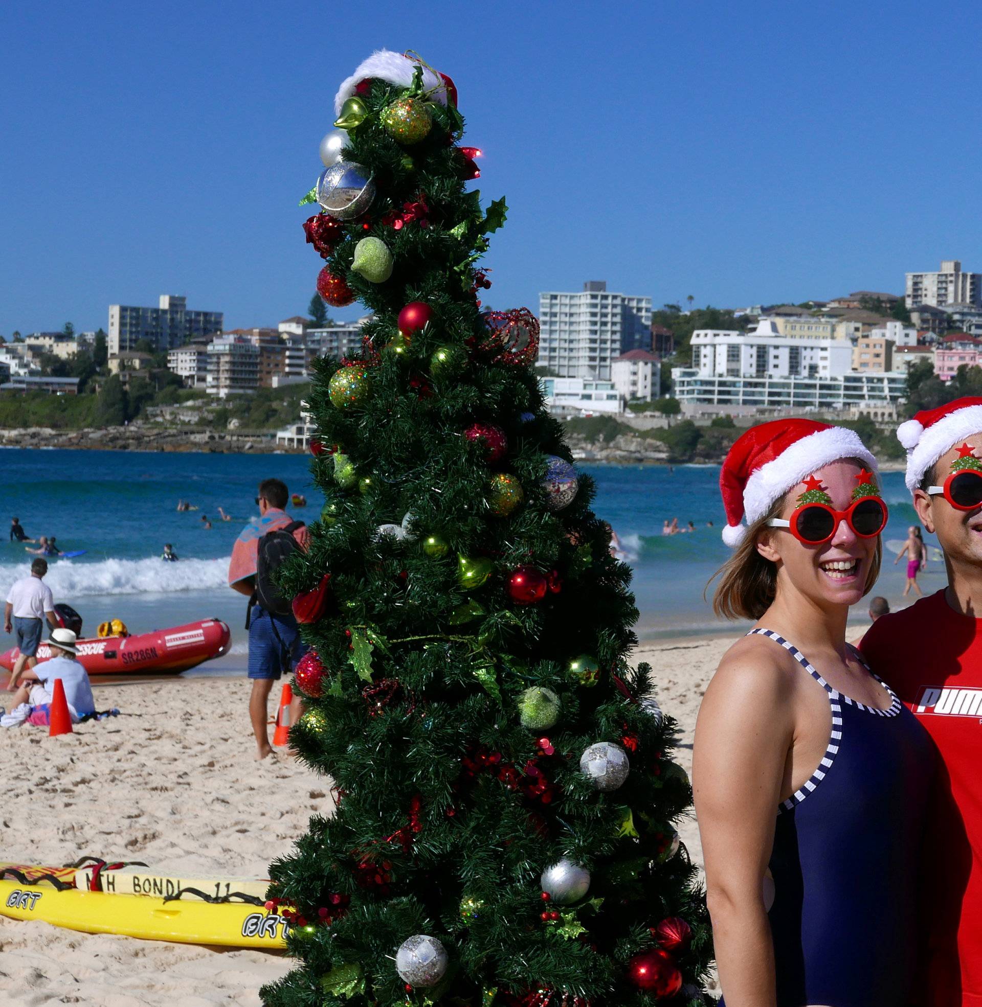 Sarah and Toby, volunteer life guards from Bondi Surf Life Saving Club, pose in front of a Christmas Tree on Bondi Beach Sydney