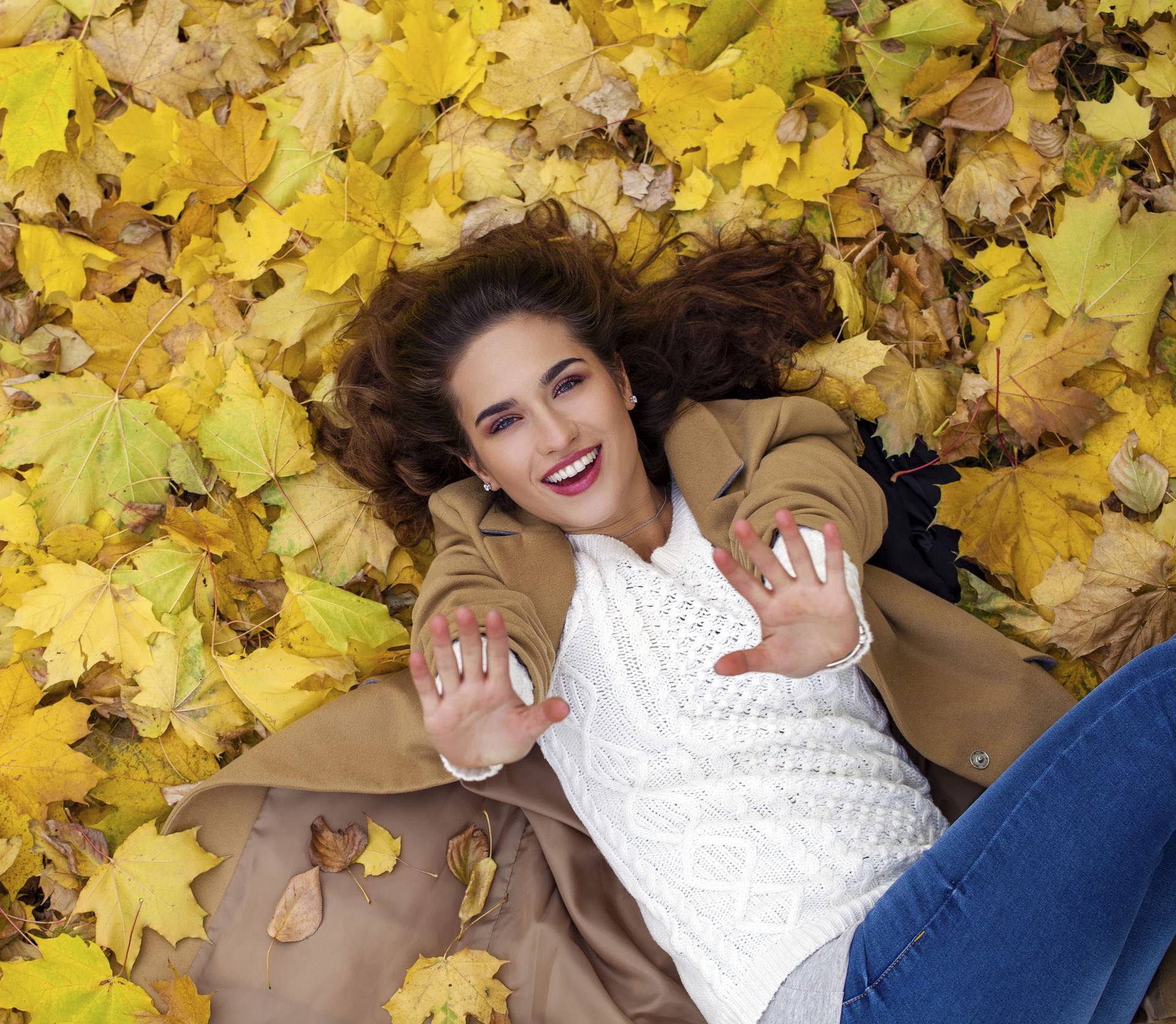 Young beautiful girl in blue jeans lying on yellow leaves