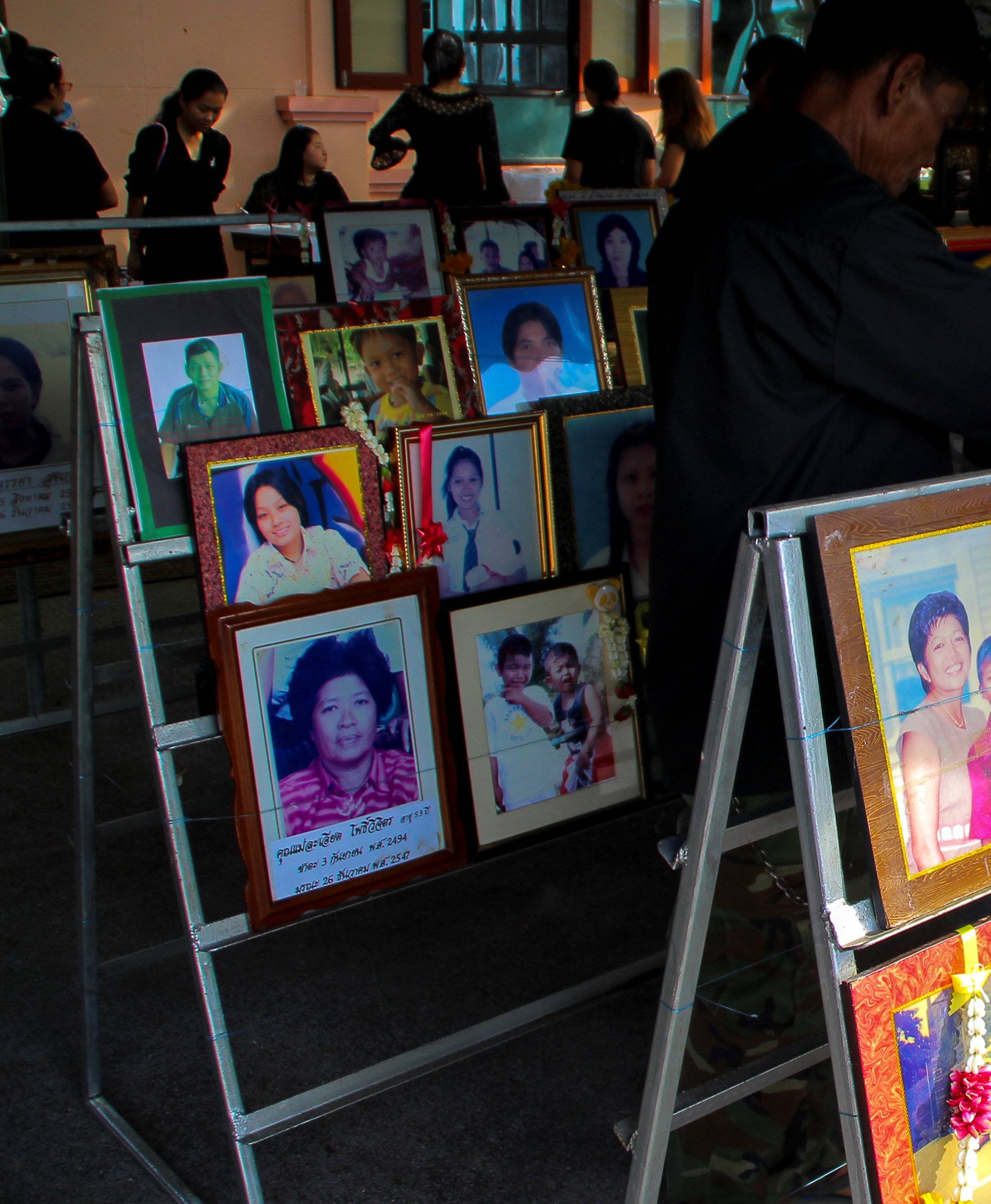 People stand next to pictures of victims of the 2004 tsunami victims during a religious ceremony in Ban Nam Khem, a southern fishing village destroyed by the wave in Phang Nga Province