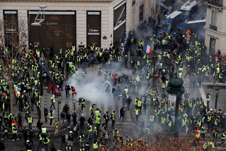 Tear gars floats in the air around protesters wearing yellow vests during clashes with French Gendarmes on the Champs-Elysees Avenue in Paris