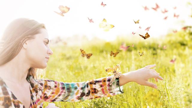 Girl sitting in a meadow in swarm of flitting butterflies.