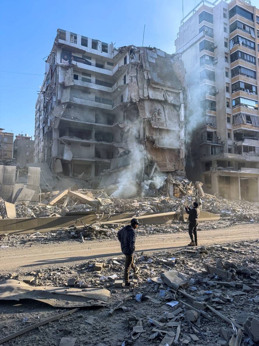 People stand on the rubble of a damaged building after an Israeli strike on Beirut's southern suburbs