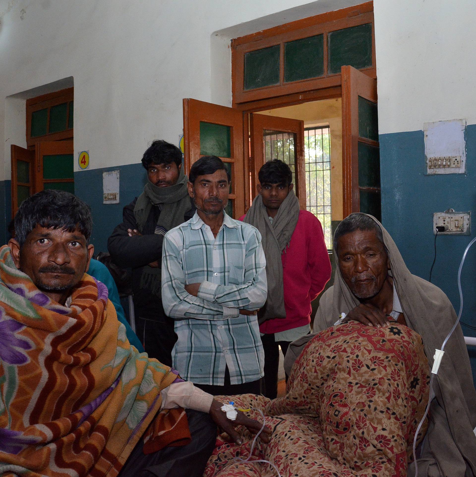 Two men who consumed bootleg alcohol, sit on a hospital bed as relatives look on, in Saharanpur