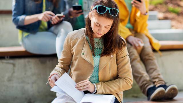 high school student girl reading book outdoors