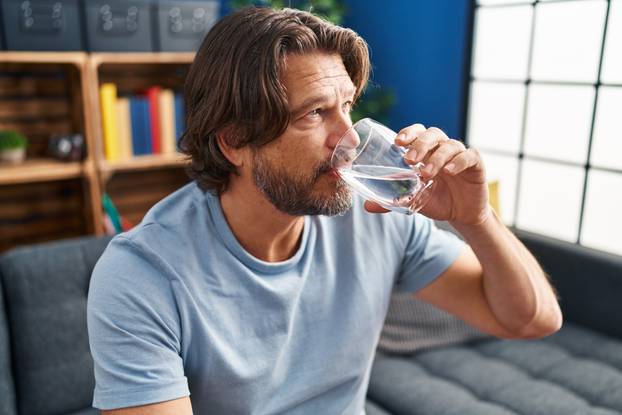 Middle,Age,Man,Drinking,Glass,Of,Water,Sitting,On,Sofa